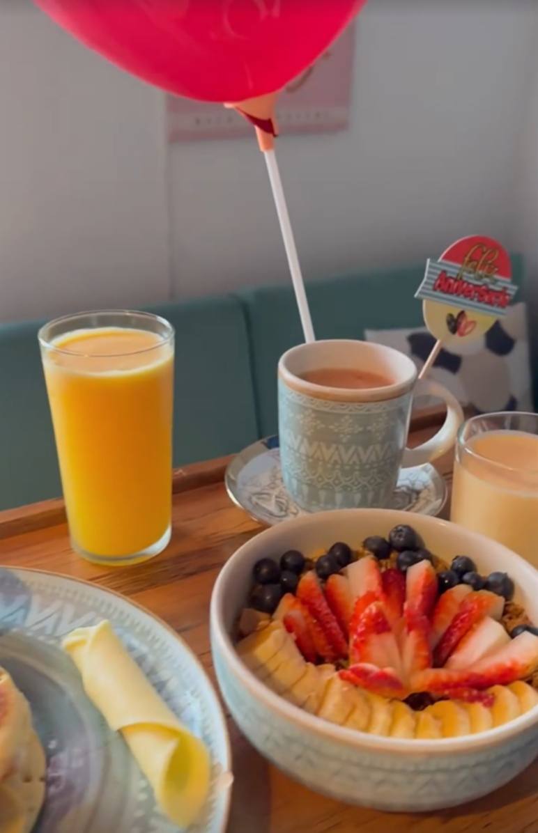 Bandeja de desayuno de celebración con bowl de frutas, jugo de naranja, café y un globo rojo.