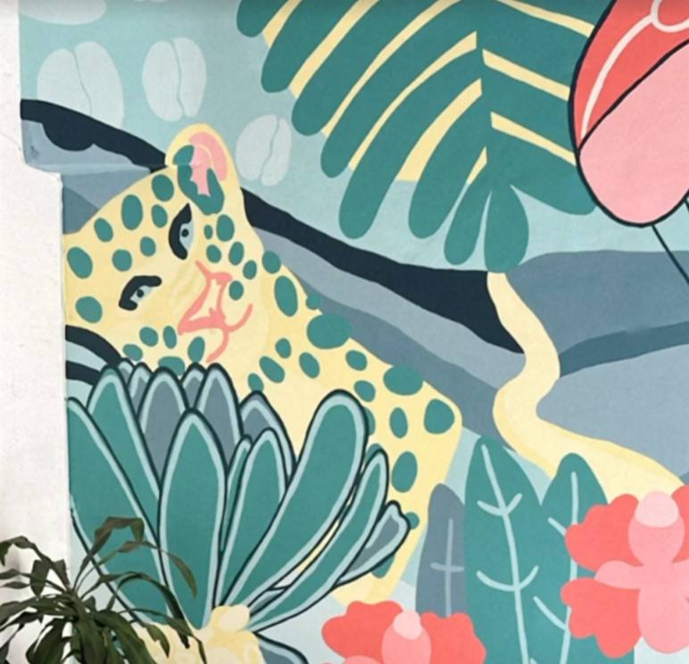 Mural de la terraza: un jaguar amarillo con manchas verdes asomado entre hojas turquesa y flores rosadas.