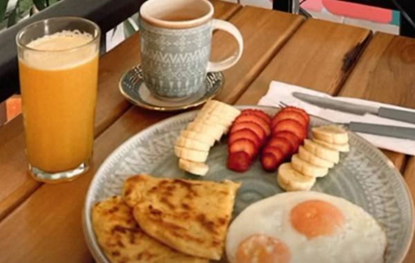 Desayuno en la mesa de madera de la terraza: arepas, huevos fritos, fresas, banano, jugo de naranja y café.