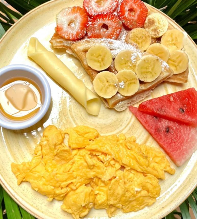Plato sobre hojas de palma: crepe con banano y fresas, huevos revueltos, sandía, queso y una salsa.